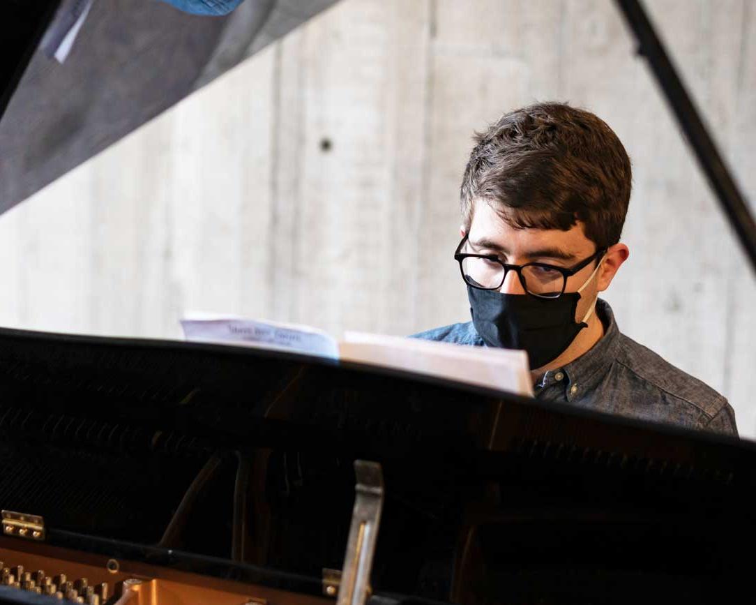 student plays a piano in front of a large window